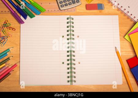 Overhead view is showing open spiral-bound notebook on wooden desk with pens, markers, calculator Stock Photo