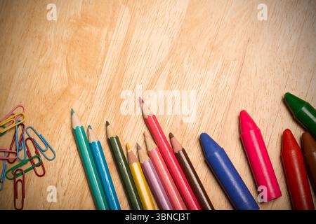 Coloring tools are lying on flat design wooden table with colored pencils, crayons, paper clips Stock Photo