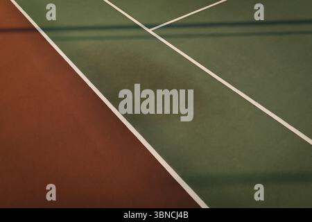 Flat-design court surface is showing brownish-red joining green with white lines and fence shadows Stock Photo