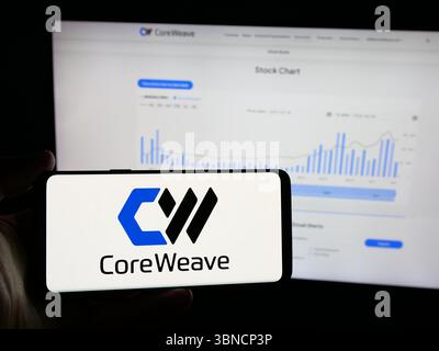 In this photo illustration, a person is holding a smartphone with the logo of US AI cloud computing company CoreWeave Inc. on screen in front of website. Stock Photo