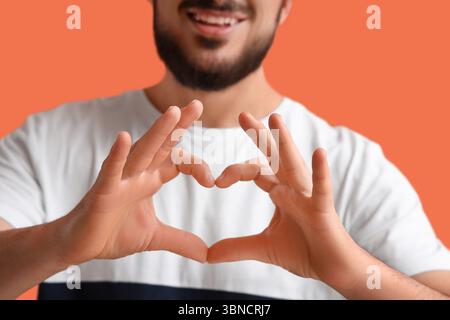 Thankful young man making heart gesture on orange background Stock Photo