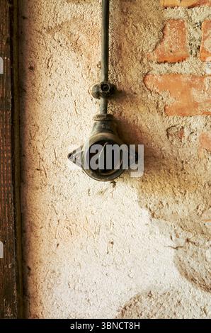 Black switch is mounted on a wall. The switch is old and rusted. The wall is made of brick and has a white base Stock Photo