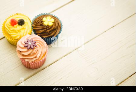 Three swirl frosting cupcakes with candy toppers are sitting on wooden plank in flat design Stock Photo