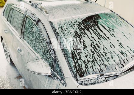 A car is being thoroughly and carefully washed, completely covered in thick, bubbly soap foam, which enhances its shine and cleanliness, making it loo Stock Photo