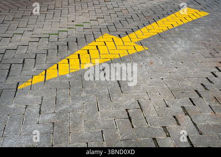 Yellow arrow is drawn on a brick sidewalk. The arrow is pointing to the right. The sidewalk is made of bricks and is located on a street Stock Photo