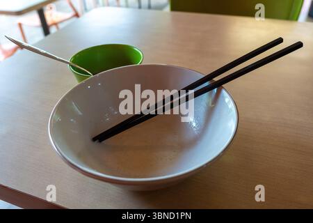 Empty bowl with chopsticks on top of it. The bowl is empty and the chopsticks are black Stock Photo