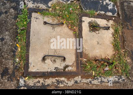 Two rusty metal pipes are sitting on a concrete slab. The pipes are covered in dirt and grass Stock Photo