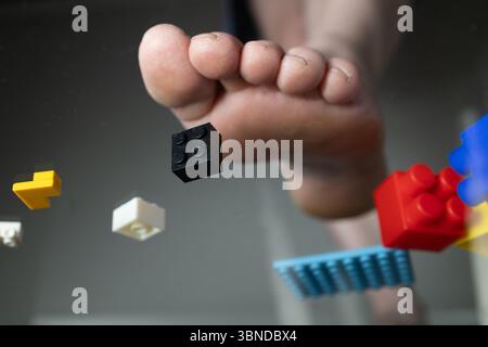 Moldova, Chisinau, July 02, 2025. A foot is about to step on various colored LEGO bricks scattered on the floor. The playful chaos of construction pieces suggests creativity and a fun building activity. Stock Photo