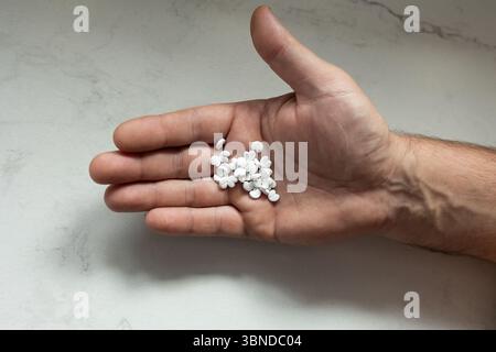 A person's hand is extended, displaying several white pills resting on a smooth, light-colored surface. The setting appears calm and neutral, possibly in a home or medical environment. Stock Photo