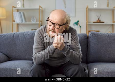 Serious Sad Senior Man Sitting On Sofa At Home Stock Photo