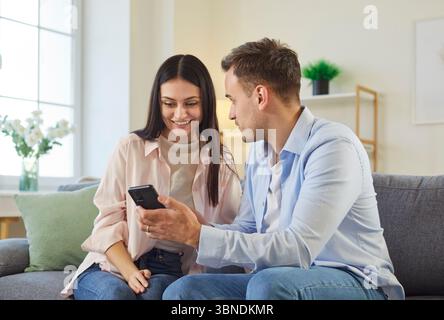 Family couple sitting together on sofa, cocncentrated at smartphone screen, watching video Stock Photo