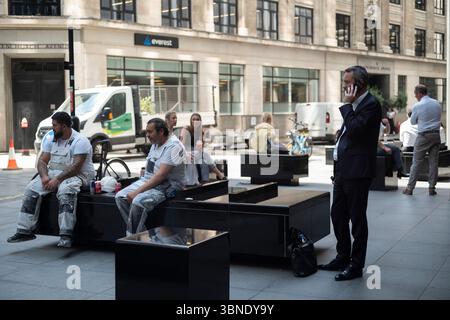 City worker taking a call on his smartphone next to manual labour workers in the heart of the financial district, City of London, England, UK Stock Photo