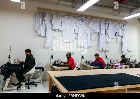Doha, Qatar - February 3, 2025: tailor asian man designer sewing clothes on sewing machine in workplace. sewing factory Stock Photo