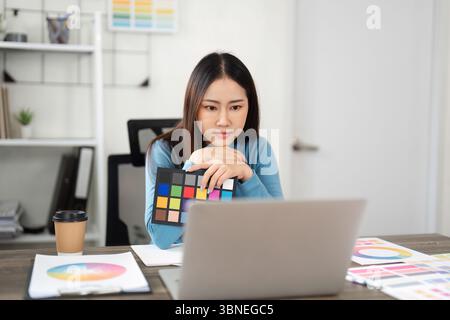 Color Theory and Design Choices. A woman analyzing color palettes on her laptop, immersed in a creative workflow. Stock Photo