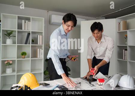 Building Plans and Collaboration. Two professionals analyzing architectural plans and discussing measurements. Stock Photo