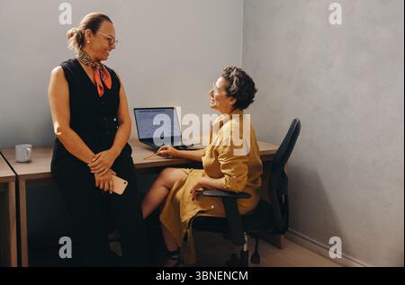 Two professional women are engaged in a collaborative discussion in a modern office. The atmosphere highlights collaboration, professionalism, and a c Stock Photo