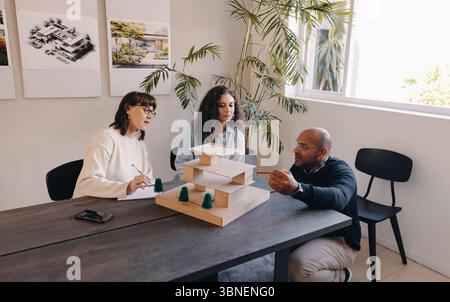 Three architects in a modern office collaborate on a project around a scale model, planning. Stock Photo