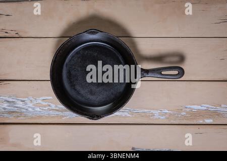 Top-down view of a small cast iron skillet with an integrated iron handle placed in center, highlighting its solid one-piece construction and texture Stock Photo