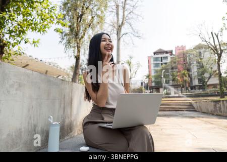 Sustainable lifestyle. Young woman enjoying her time outdoors while working on a laptop and smiling. Stock Photo
