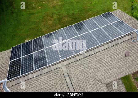 Close-up angle showing modern solar panels installed on an asphalt-shingle roof with tree-lined background. Stock Photo