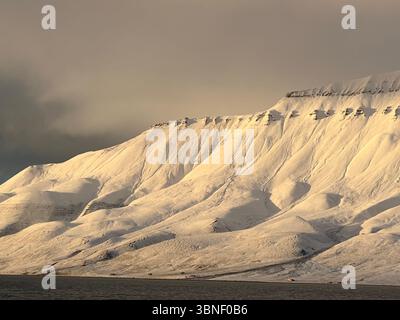Snowy mountains dominate the landscape under a cloudy sky in Longyearbyen, Svalbard Stock Photo