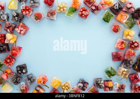 Frame of ice cubes with frozen berries and fruits and mint on blue background Stock Photo
