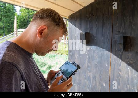 Man Controlling Drone with Remote and Screen. Close-up of a man operating a drone using a handheld remote controller with a mounted screen, standing Stock Photo