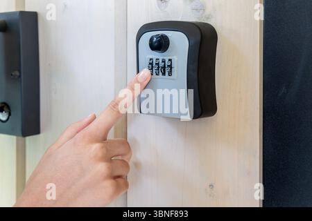 Hand Entering Code on Wall-Mounted Lockbox. Close-up of a person entering a numeric code on a combination key lockbox mounted to a wooden wall for Stock Photo