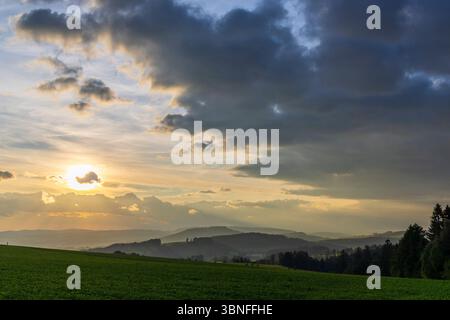 Sun setting behind clouds over rolling hills in Chvalec, Czechia Stock Photo