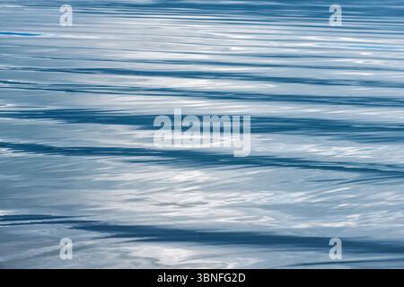 Soft ripples create a pattern on the clear blue water under the midday light, showcasing a serene lakeside atmosphere. Stock Photo