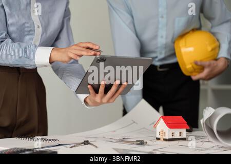 Collaboration and Construction Planning. Professionals discussing architectural plans while using a tablet for project management. Stock Photo