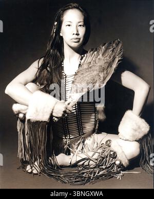 Young woman in native American clothes sitting cross-legged in studio. Stock Photo
