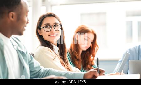 International group of smiling students sitting at desk and talking Stock Photo
