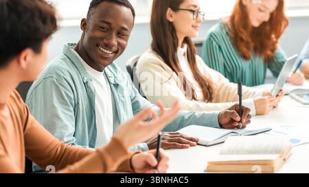 Diverse group of students sitting at desk writing and talking Stock Photo