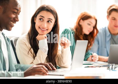Smiling diverse students sitting at desk working on group project Stock Photo