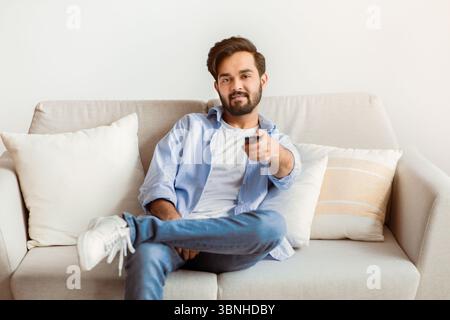 Smiling Young Middle Eastern Guy Watching TV At Home. Stock Photo