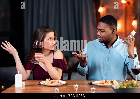 Young Woman Complaining About Her Boyfriend Talking On Cellphone During Romantic Date Stock Photo