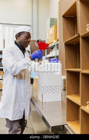 Worker sealing cardboard boxes with tape in food processing warehouse. Stock Photo