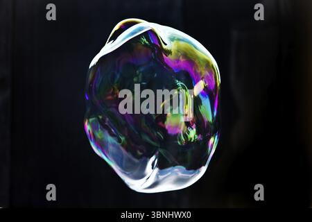 A large iridescent and floating soap bubble in the colours of the rainbow against a black background, Recklinghausen, Germany, Europe Stock Photo