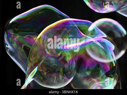 Large, irregular, iridescent soap bubbles in the colours of the rainbow against a black background, Recklinghausen, Germany, Europe Stock Photo