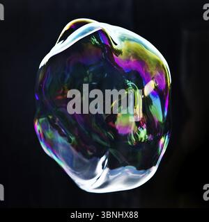 A large iridescent and floating soap bubble in the colours of the rainbow against a black background, Recklinghausen, Germany, Europe Stock Photo