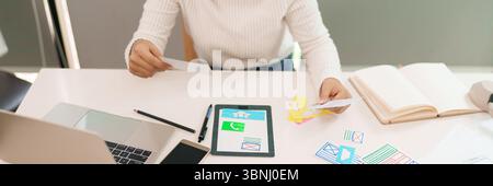 Asian young woman is designing a mobile app layout with hand holding paper ideas and website design. Sketching User Experience process on the table wi Stock Photo