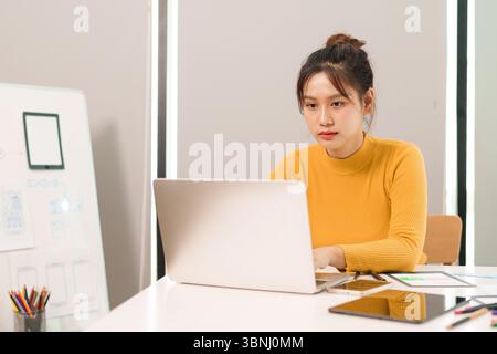 An adult Asian women UI UX designer focused on designing a user interface for mobile app and web. She is prototyping and wireframing on laptop at her Stock Photo
