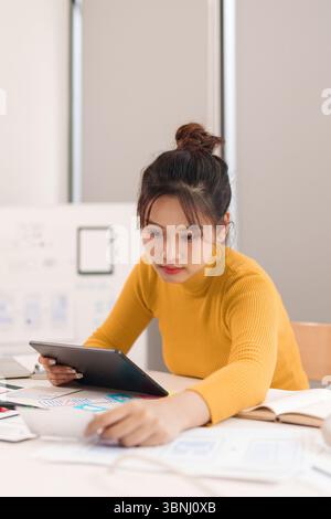 Young Asian woman UI UX designer working on her app design project with a tablet. Female focused on user interface design development and website crea Stock Photo
