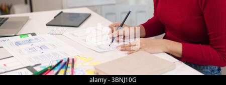 An adult Asian women UI designer is sketching mobile app interface design on paper with a pencil at the office for website and application project. Stock Photo