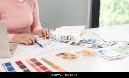 Young Asian woman interior designer is working on color selection for website or application project with laptop on the table. Planning user experienc Stock Photo