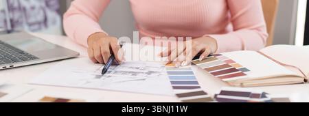 Asian adult woman's hands are sketching architectural plans with a pen color palettes laptop and notebook in her creative office showing interior desi Stock Photo