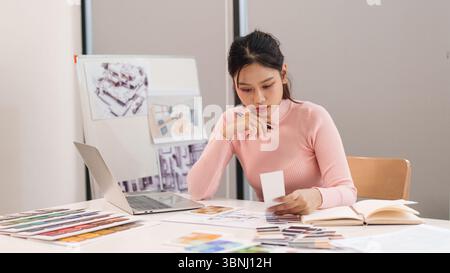 An Asian young adult woman using color swatches for design project planning. She works as UI UX designer creating interfaces for web and mobile applic Stock Photo