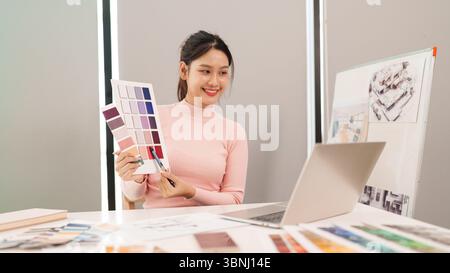 Adult Asian woman user interface designer presents color samples for website design during a video conference. Working on a computer for an online mee Stock Photo