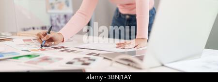 An adult Asian woman interior designer is working on a home decor project. She is choosing a color palette and creating a design using a laptop. She i Stock Photo